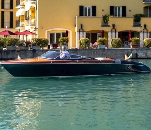 Luxurious RIVA Aquariva speedboat docked in front of charming, sunlit buildings by the calm waters. Ideal for those seeking unique and exclusive rental experiences, this elegant vessel combines modern luxury with classic Italian design. Explore scenic destinations and enjoy an unforgettable journey aboard a RIVA speedboat, tailored to your desires and guided by our professional captains