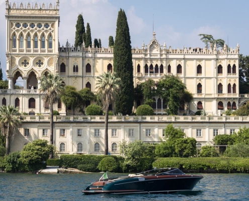 Riva Aquariva cruising on Lake Garda with Isola del Garda and its neo-Gothic villa in the background.