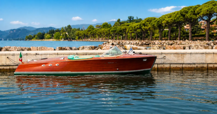 Vintage Riva boat on Lake Garda with elegant shoreline and crystal clear water, luxury private boat rental experience