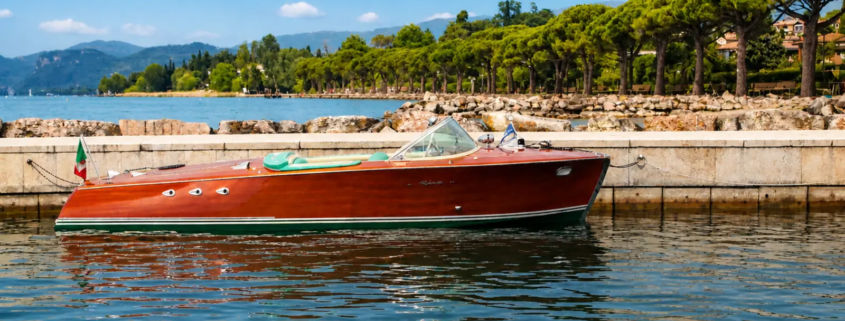 Vintage Riva boat on Lake Garda with elegant shoreline and crystal clear water, luxury private boat rental experience